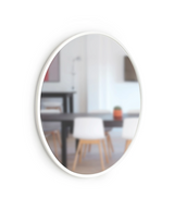 A versatile Umbra HUB WALL MIRROR - White 94cm hangs elegantly on a wall, complemented by a sturdy table and chairs.