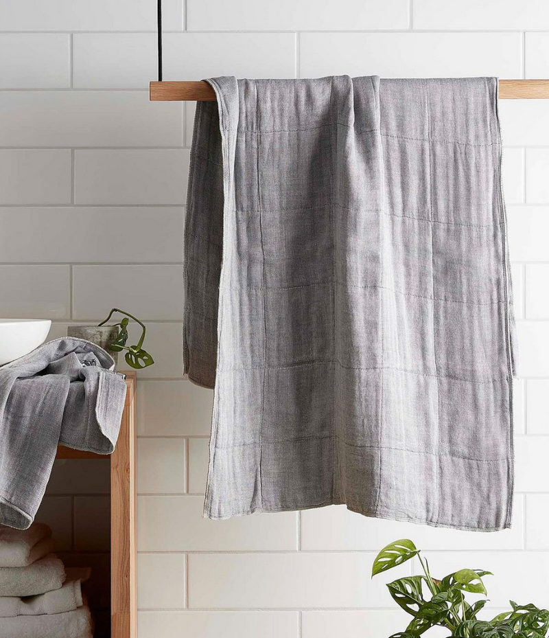 An organic face towel hangs on a wooden rack in a bathroom, bearing the brand name Nawrap.