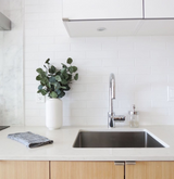 A white kitchen with Nawrap antibacterial wooden cabinets and a plant on the counter.