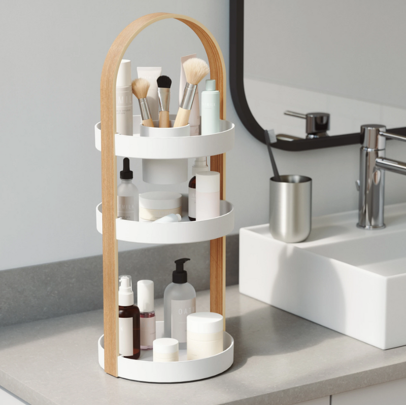 An Umbra BELLWOOD COSMETIC ORGANIZER with a three tier wooden shelf for cosmetics, makeup brushes, and other bathroom essentials.