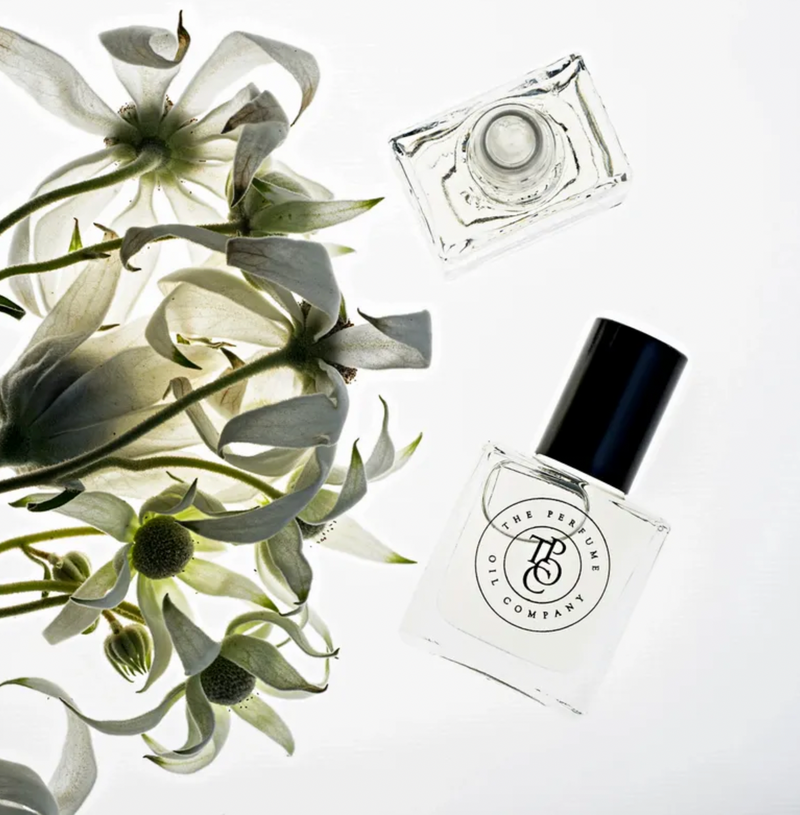 A bottle of The Perfume Oil Collection Gift Set - Fresh by The Perfume Oil Company next to a bouquet of white flowers, featuring floral fragrances.