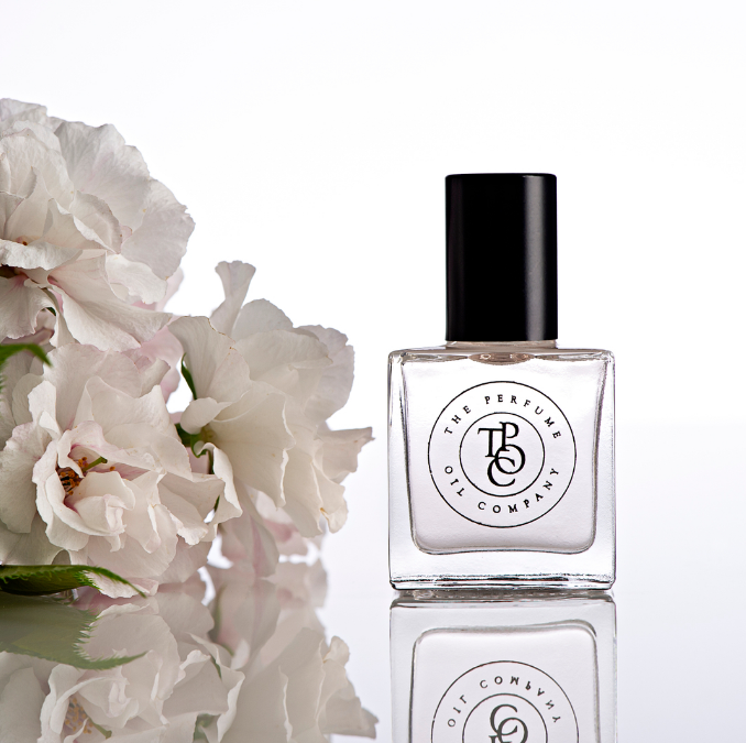 Perfume oil bottle beside soft white roses
