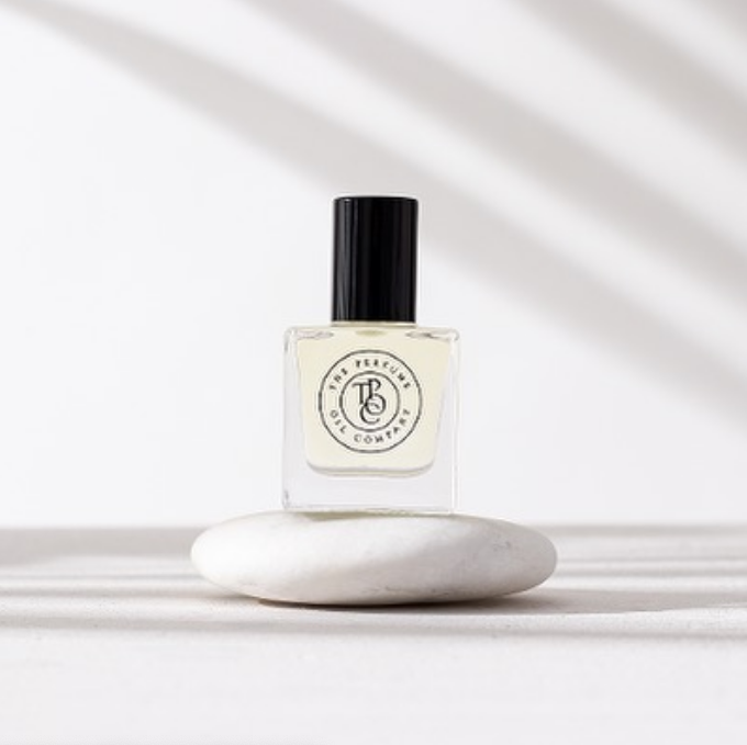 A bottle of AFRIQUE perfume inspired by Bal d'Afrique by Byredo, sitting on top of a white stone. (Brand Name: The Perfume Oil Company)