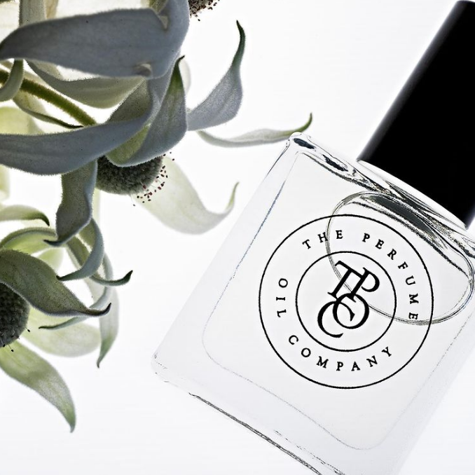 Close view of a perfume oil bottle label beside grey-green leaves