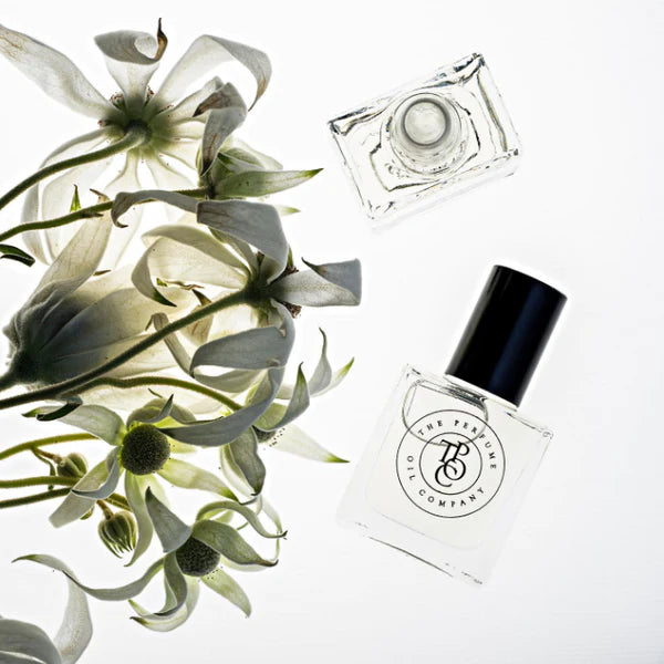 A bottle of CALYPSO perfume, inspired by Mango Skin from Vilhelm Parfumerie, next to a bouquet of white flowers.