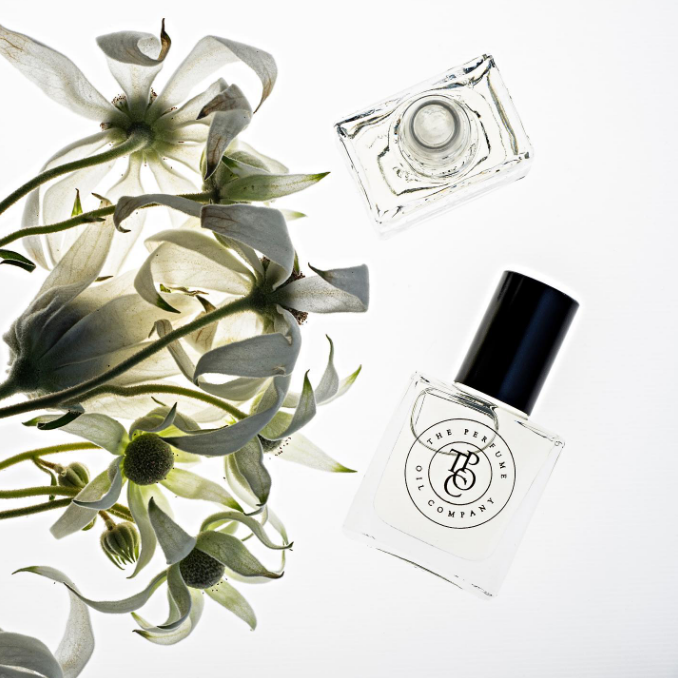 A bottle of AFRIQUE perfume, inspired by Bal d'Afrique (Byredo), next to a bouquet of white flowers.