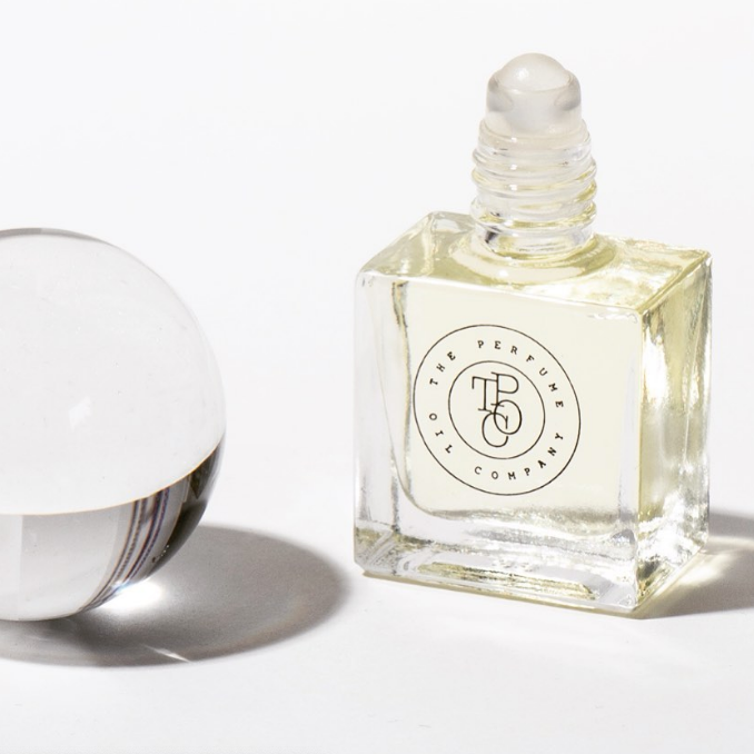 Perfume oil roll-on bottle beside a clear glass sphere on white