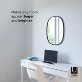 A room with a desk, chair, and an Umbra Hub Mirror Oval - Black with a rubber rim.