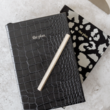 A limited edition Papier HQ black crocodile skin notebook from the Papier HQ stationery range, complete with a Brass Reusable Pen on top.
