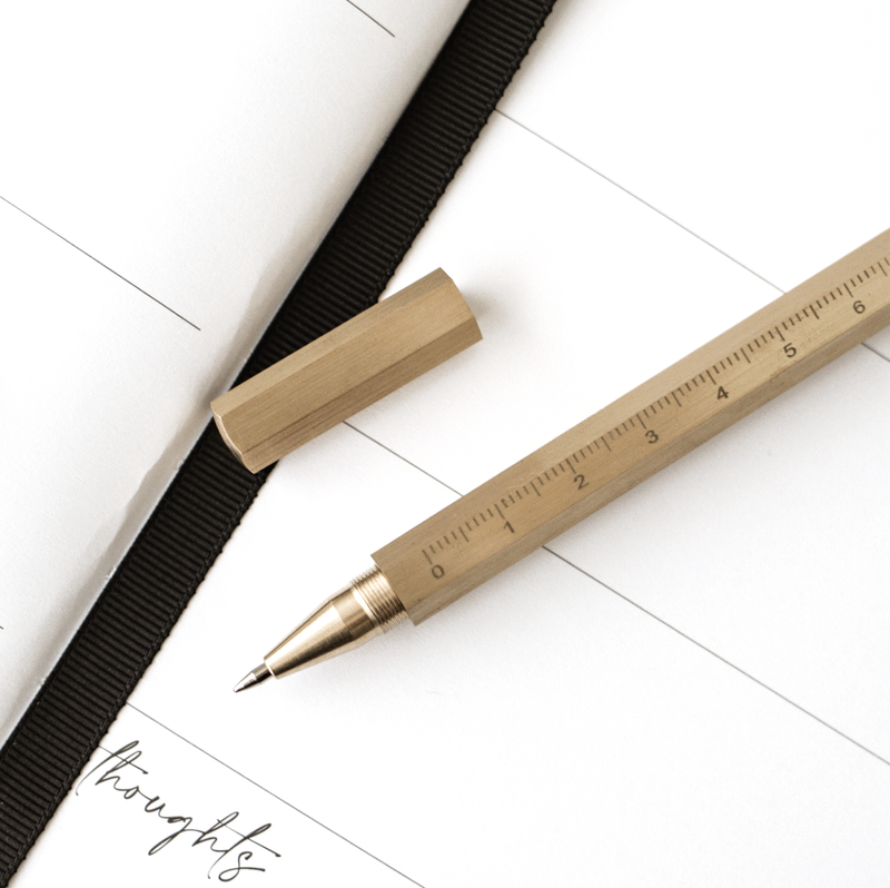 A limited edition Brass Reusable Pen with a ruler on top of a notebook from Papier HQ's stationery range.