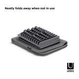 A black tray with the words neatly folds away like a mat when not in use, utilizing the Umbra UDRY PEG DRYING RACK WITH MAT's peg system.