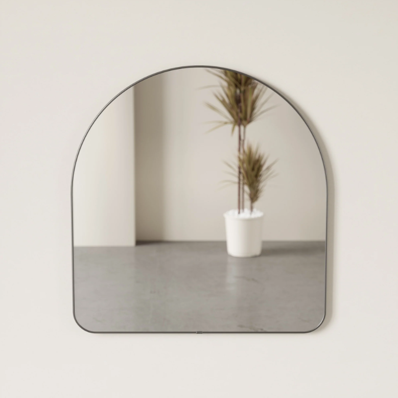 Umbra Hubba arched mirror in titanium on a pale wall reflecting a potted plant