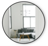 A modern round mirror, specifically the Umbra Hub Mirror - Large, in a living room.