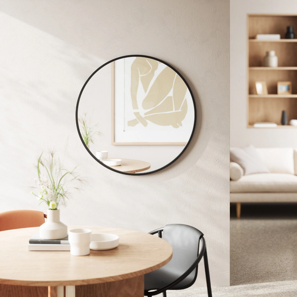 A modern Umbra Hub Mirror - Large hangs above a table in a living room.