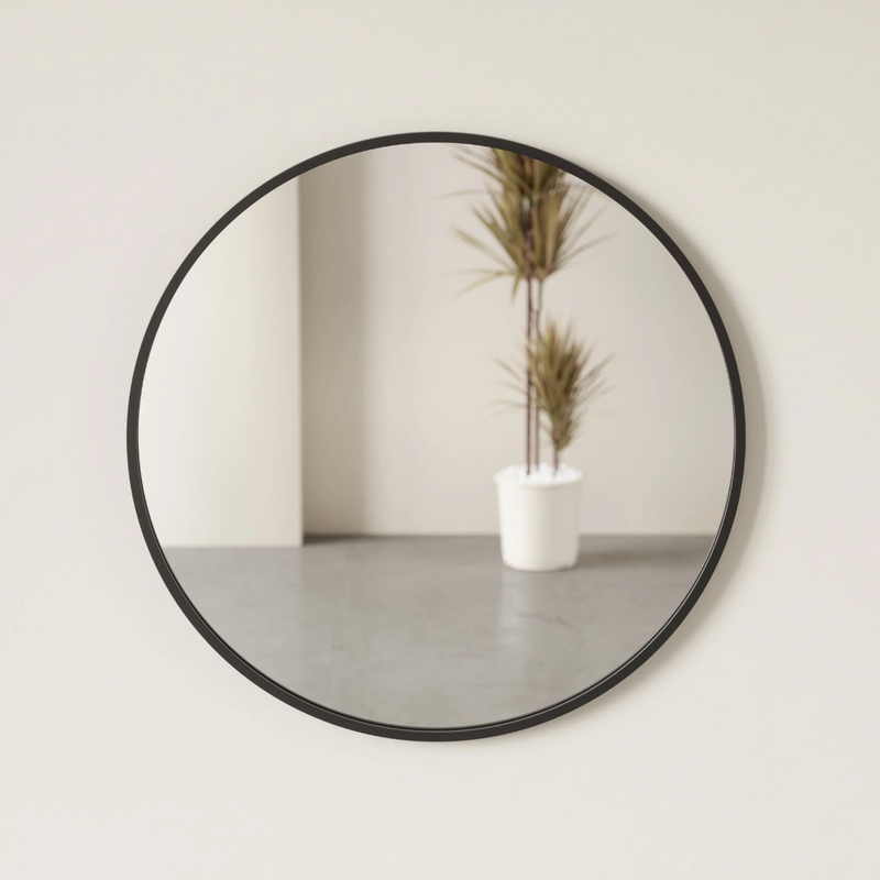 A modern round mirror, named HUB MIRROR - Large from the brand Umbra, hangs on the wall alongside a vibrant potted plant.