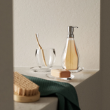 A bathroom with a toothbrush, soap, and a glass of water featuring the Droplet Tumbler / Toothbrush Holder - Clear from the Umbra Design Bath Accessory Collection.