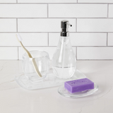 A glass tray with an Umbra DROPLET SOAP PUMP, CLEAR toothbrush and a Droplet Soap Pump.