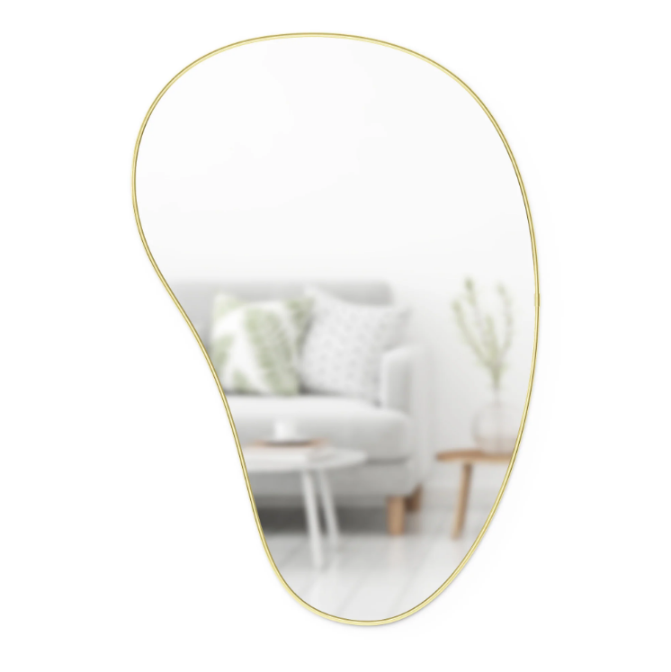 Umbra Hubba Pebble Mirror in brass reflecting a white sofa and a potted plant