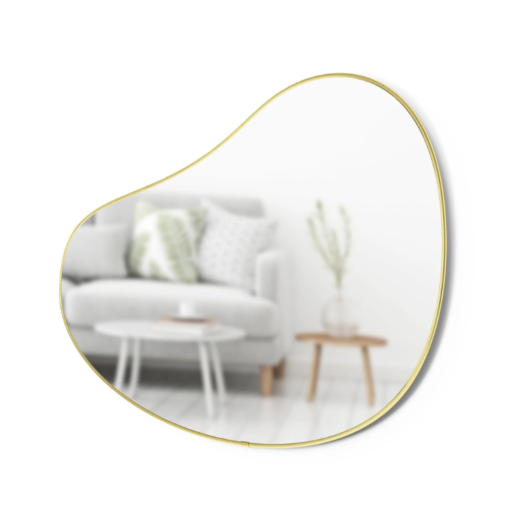 Umbra Hubba Pebble Mirror hung on the wall of a living room, reflecting natural light.