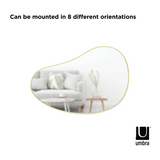 A HUBBA PEBBLE MIRROR with an organic shape and a metallic finish that can be mounted in different orientations, branded by Umbra.