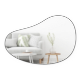 An Umbra HUBBA PEBBLE MIRROR with a metallic finish hangs in a living room, alongside a comfortable couch and trendy coffee table.