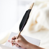A woman writing in a notebook with an AXEL & ASH Black Feather Pen, capturing her thoughts and ideas elegantly.