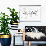 A wanderlusting soul's living room adorned with a black Let's See It All couch from AXEL & ASH and gold potted plants.