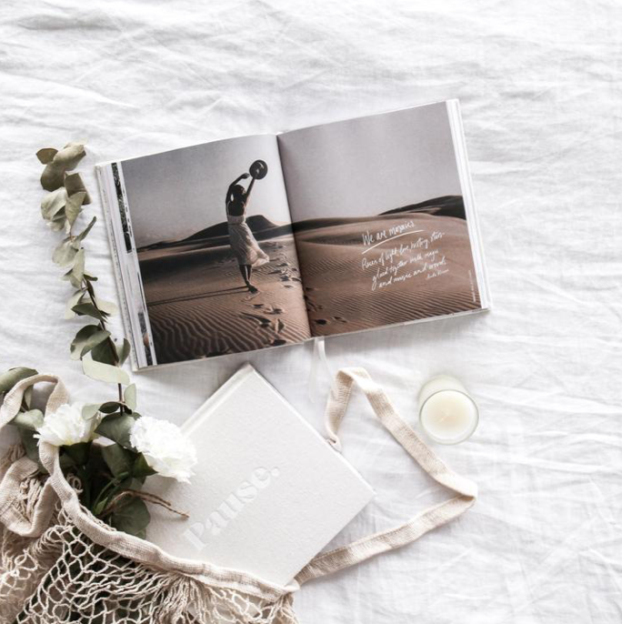 Pause guided journal in linen with a net bag, white flowers, an open book and a candle on crumpled white linen