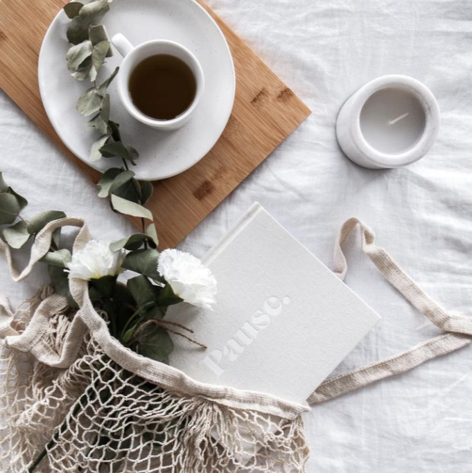 Press Pause journal on crumpled linen with a mesh bag, white flowers, coffee and a candle