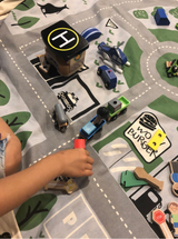 A child engaging in imaginative play with the Play Pouch Wow Town Track Interactive, filled with a toy city on a rug.