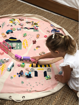 A little girl enjoying interactive play with a pink Raindrops Village - Interactive Play Pouch.