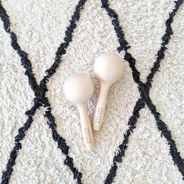 Two Jaclyn and Matisse Wooden Maraca Pairs on top of a rug.