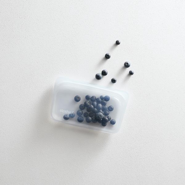 Clear Stasher snack bag filled with blueberries, more berries scattered beside it