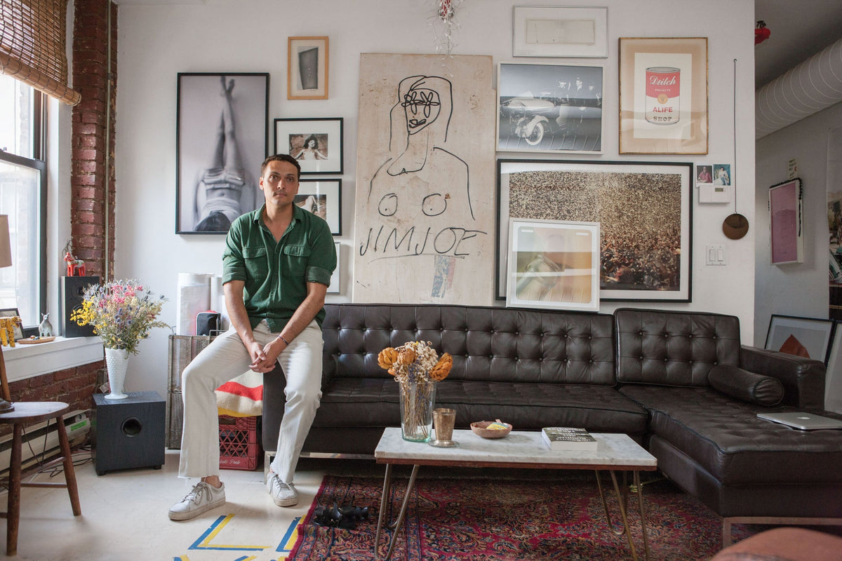 An artistic man sitting on a couch reading "Surf Shacks: An Eclectic Compilation Of Creative Surfers Homes From Coast To Coast and Overseas" by Books in a surfers' home.