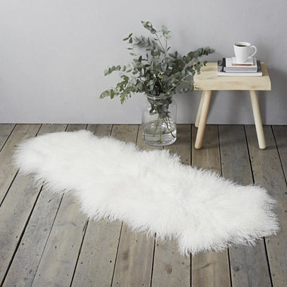 White Tibetan lamb fur rug on a weathered timber floor beside a stool and a vase of eucalyptus