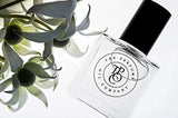 A cruelty-free SASS roll-on perfume oil inspired by Black Opium (YSL) next to a flower. (Brand: The Perfume Oil Company)
