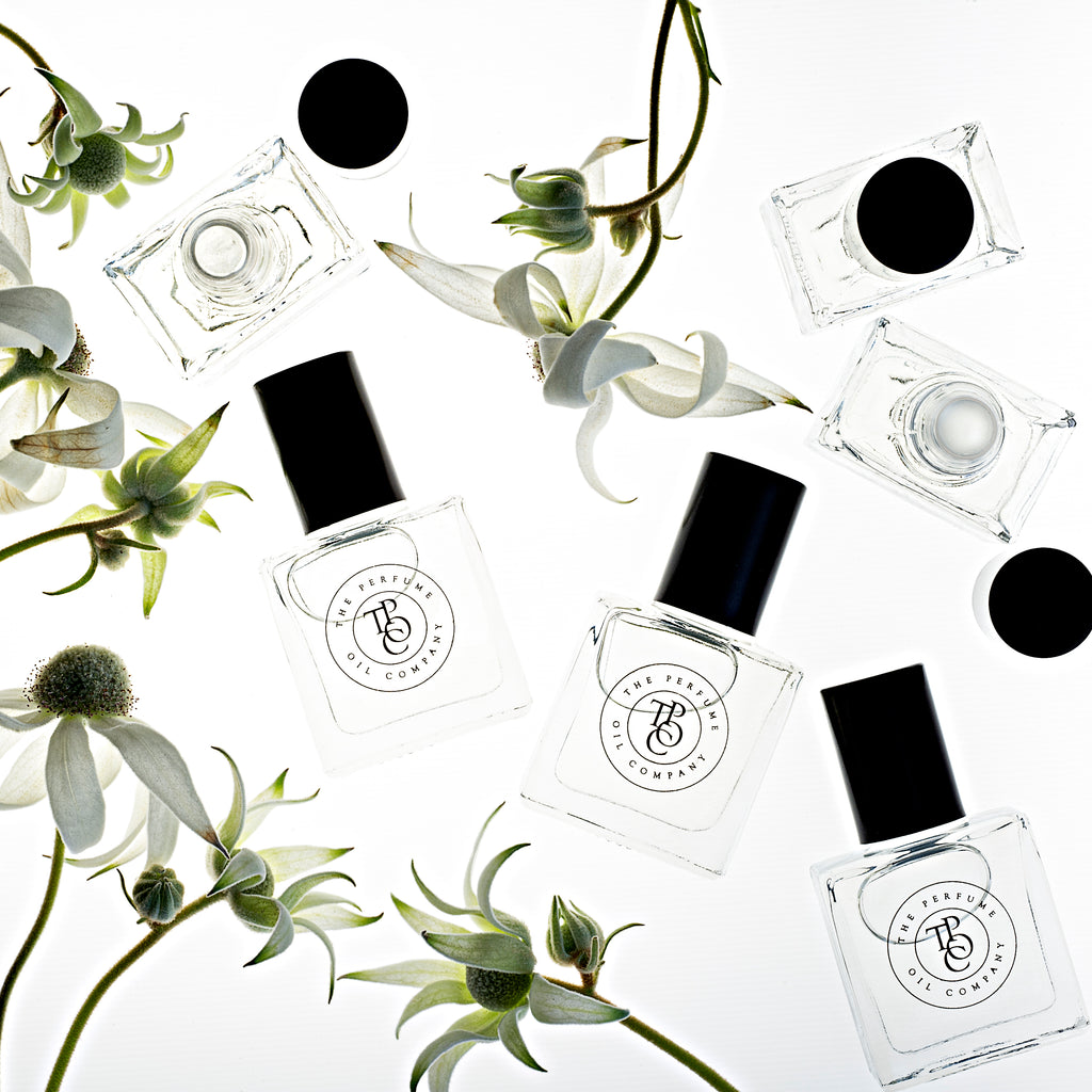 Flat lay of perfume oil bottles and black caps with white flowers