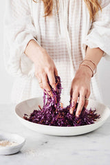 The Beauty Chef Gut Guide is slicing red cabbage in a bowl, promoting gut health.