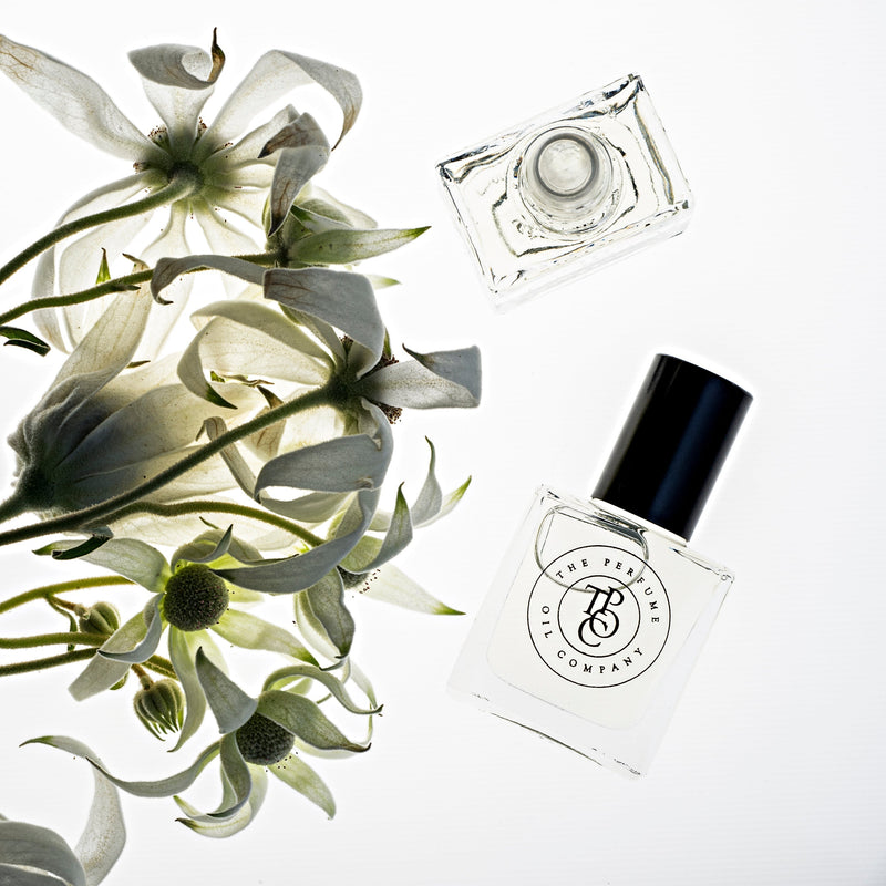 A bottle of BLEU perfume by The Perfume Oil Company next to a bunch of white flowers.