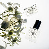 A bottle of WOODLAND perfume by The Perfume Oil Company and flowers on a white surface.