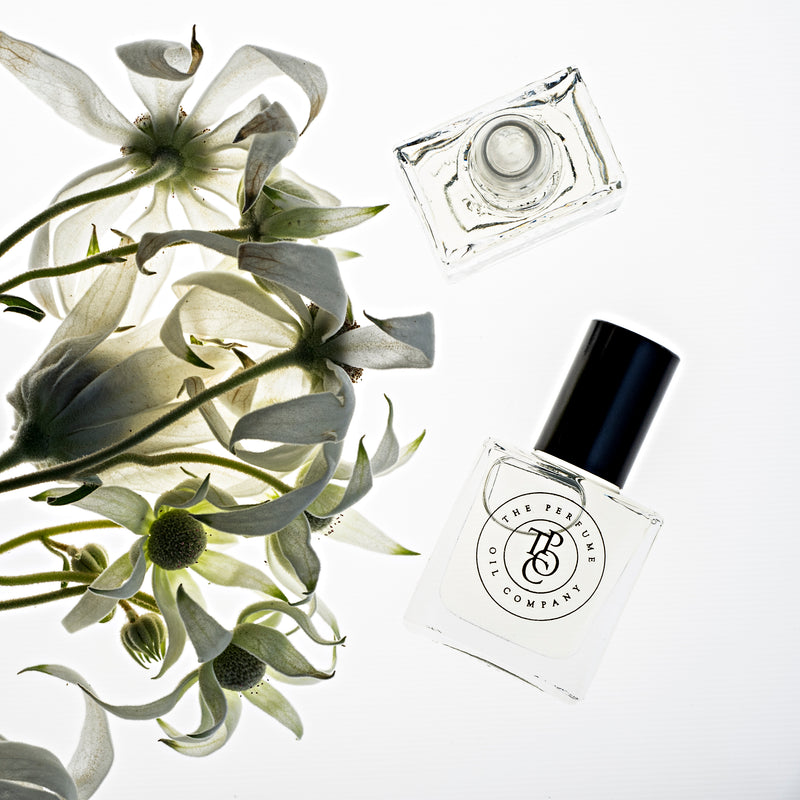A bottle of PASSION, inspired by Mon Paris (YSL) from The Perfume Oil Company next to a bunch of white flowers.
