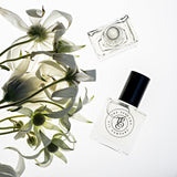A bottle of TULIP perfume, inspired by La Tulipe (Byredo), next to a bunch of white flowers.