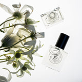 A bottle of LUSH fragrance, inspired by Be Delicious (DKNY), next to a bunch of white flowers.