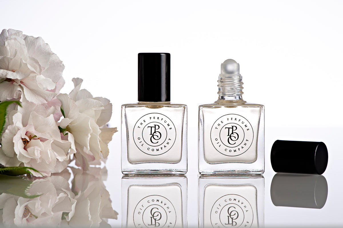 Two perfume oil bottles beside pale roses with a cap lying in front