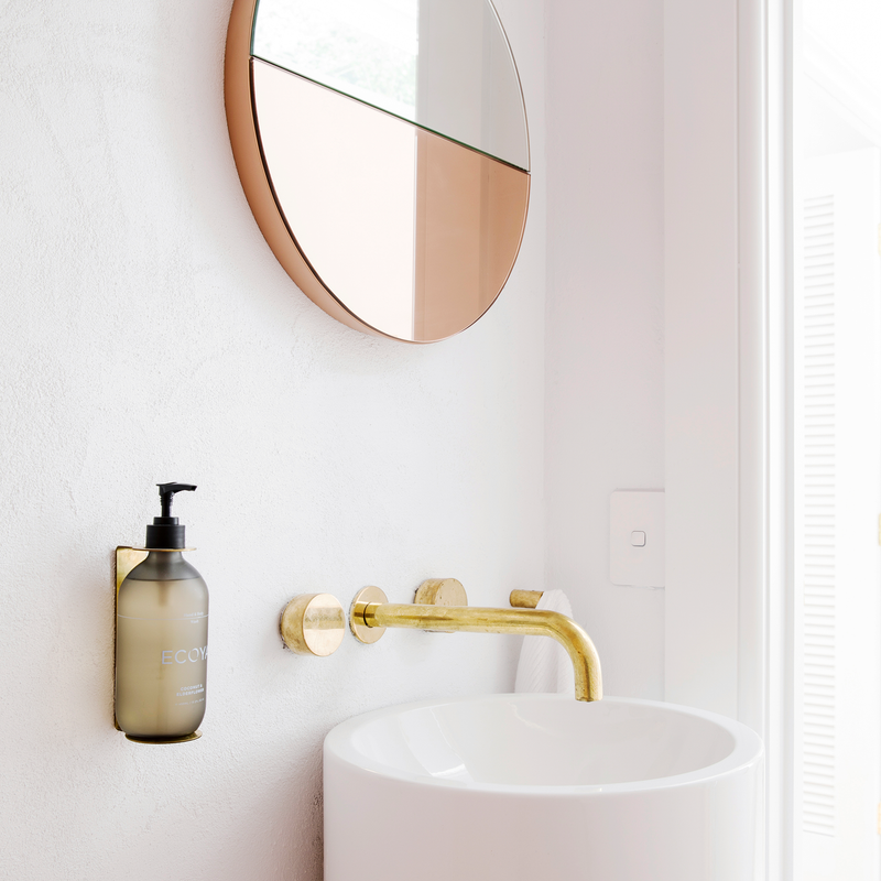 A scandinavian-inspired bathroom with a white fragranced hand and body wash sink and a gold mirror from Ecoya reflecting stunning design.