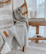 A wicker chair with a Ribbed Tassel Throw | Grey made of Oeko-tex® Certified Cotton. Brand name: Bengali Collections.