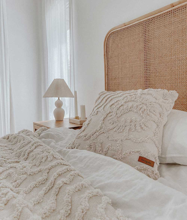 A white bed with a wicker headboard and Oeko-tex® certified Bengali Collections pillows featuring the IVORY TUFTED CUSHION COVER.