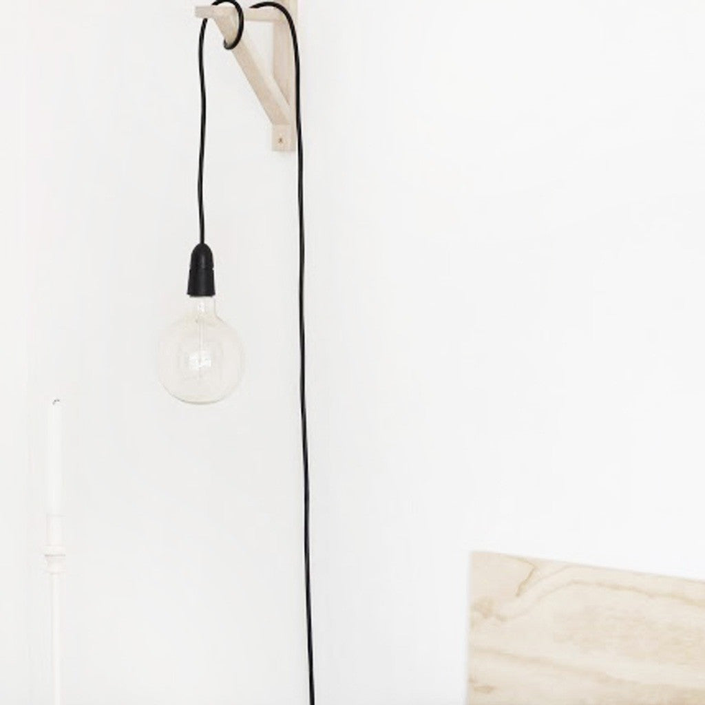 Black plug-in pendant cord hung from a timber wall hook with a clear bulb