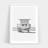 A black and white photo of a lifeguard tower on the beach, available for Number 5 by Art Prints.