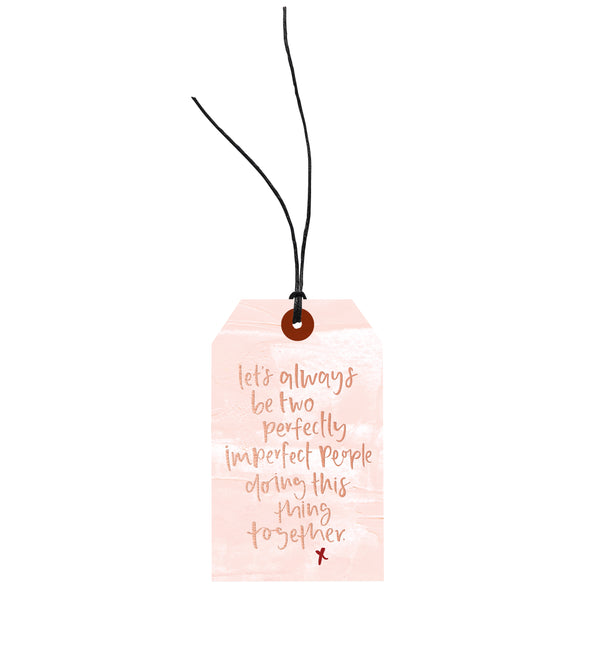 A pink Let's Always Be Two Imperfect People tag with a quote on it, perfect for adding a touch of elegance and sentiment to any gift.